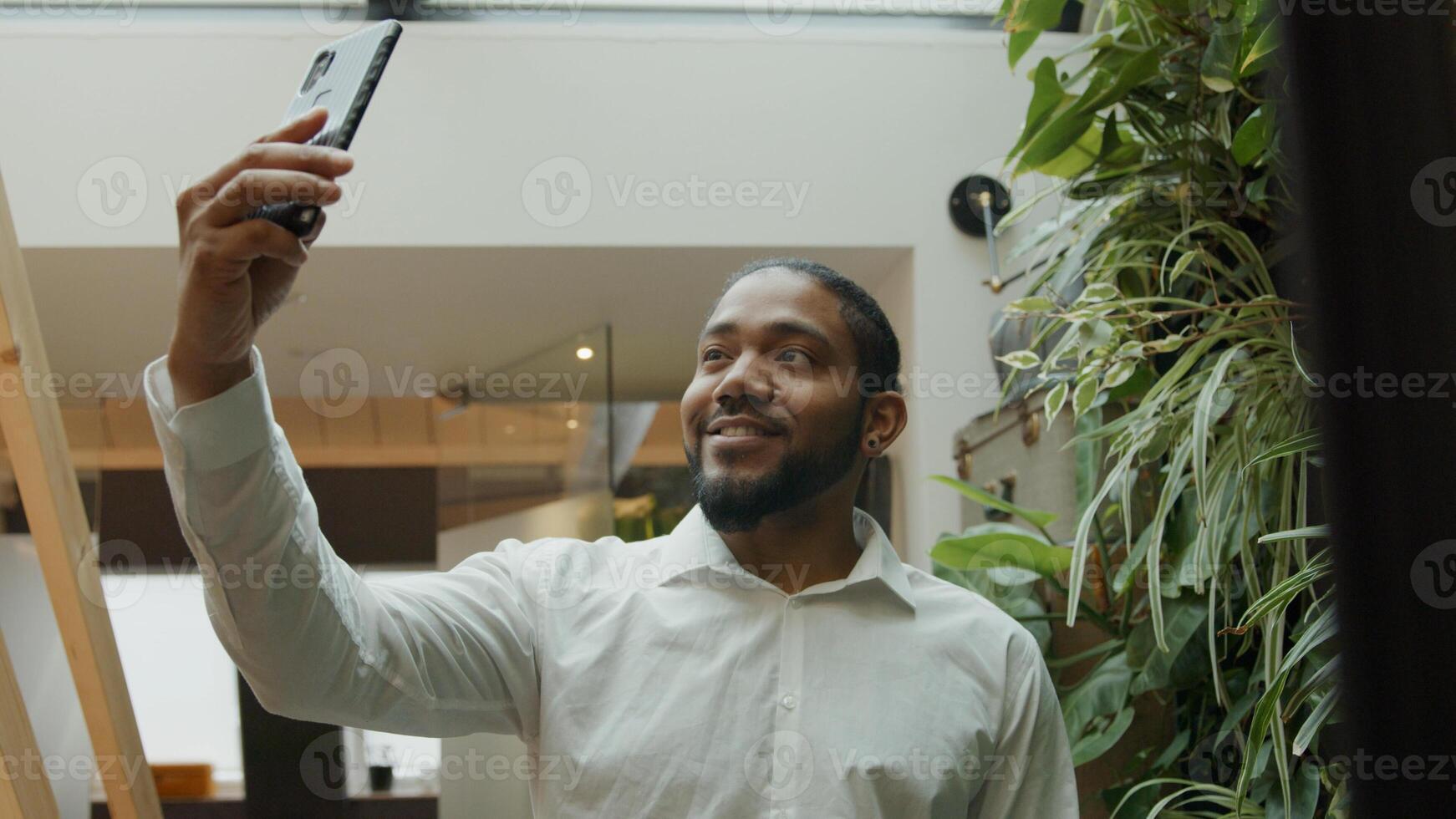 Black man standing, holding mobile phone in the air, following himself making video, smiling photo