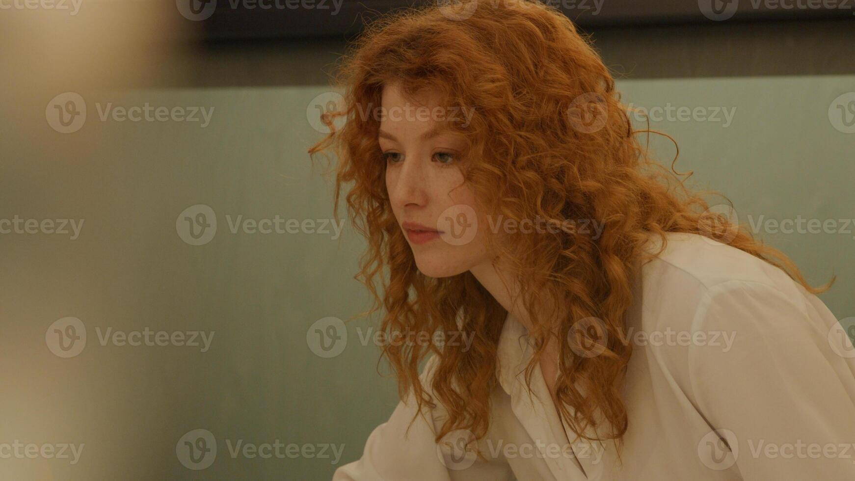 White young woman and black mature woman sitting at table in office, white woman points, black woman watches photo