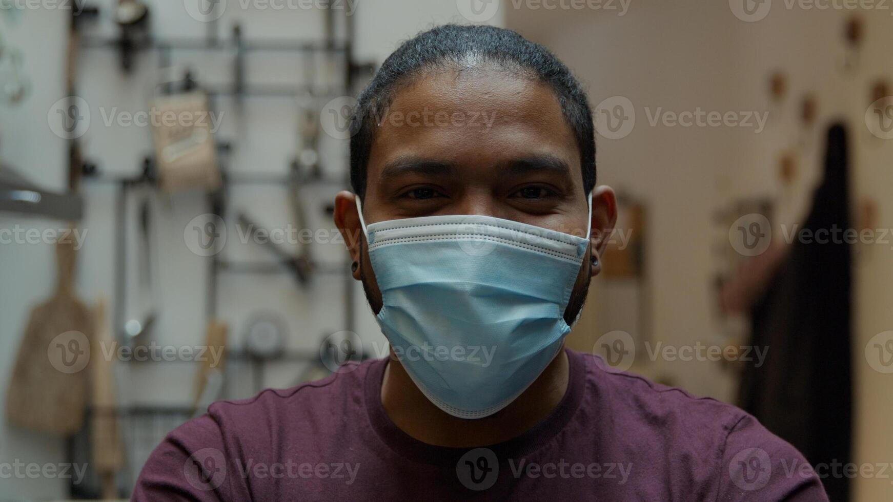 Close up of black man, looks into camera lens, smiling, puts on face mask with both hands, adjusting mask, laughing eyes photo