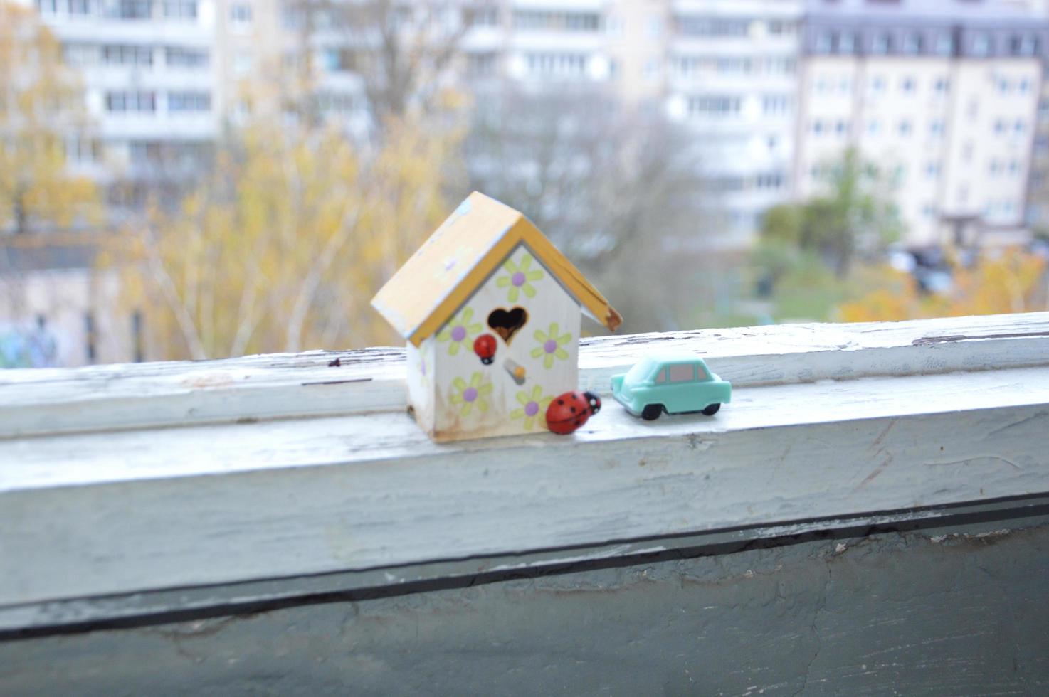 A small house stands on a balcony windowsill against a background of autumn photo