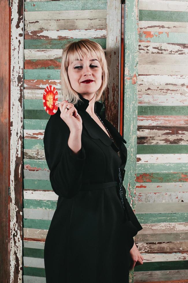 pretty blonde in black dress holding a stick of red candy photo