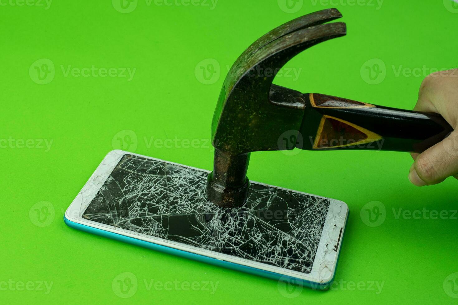 Hand holding Hammering the phone smartphone screen is cracked on green background photo