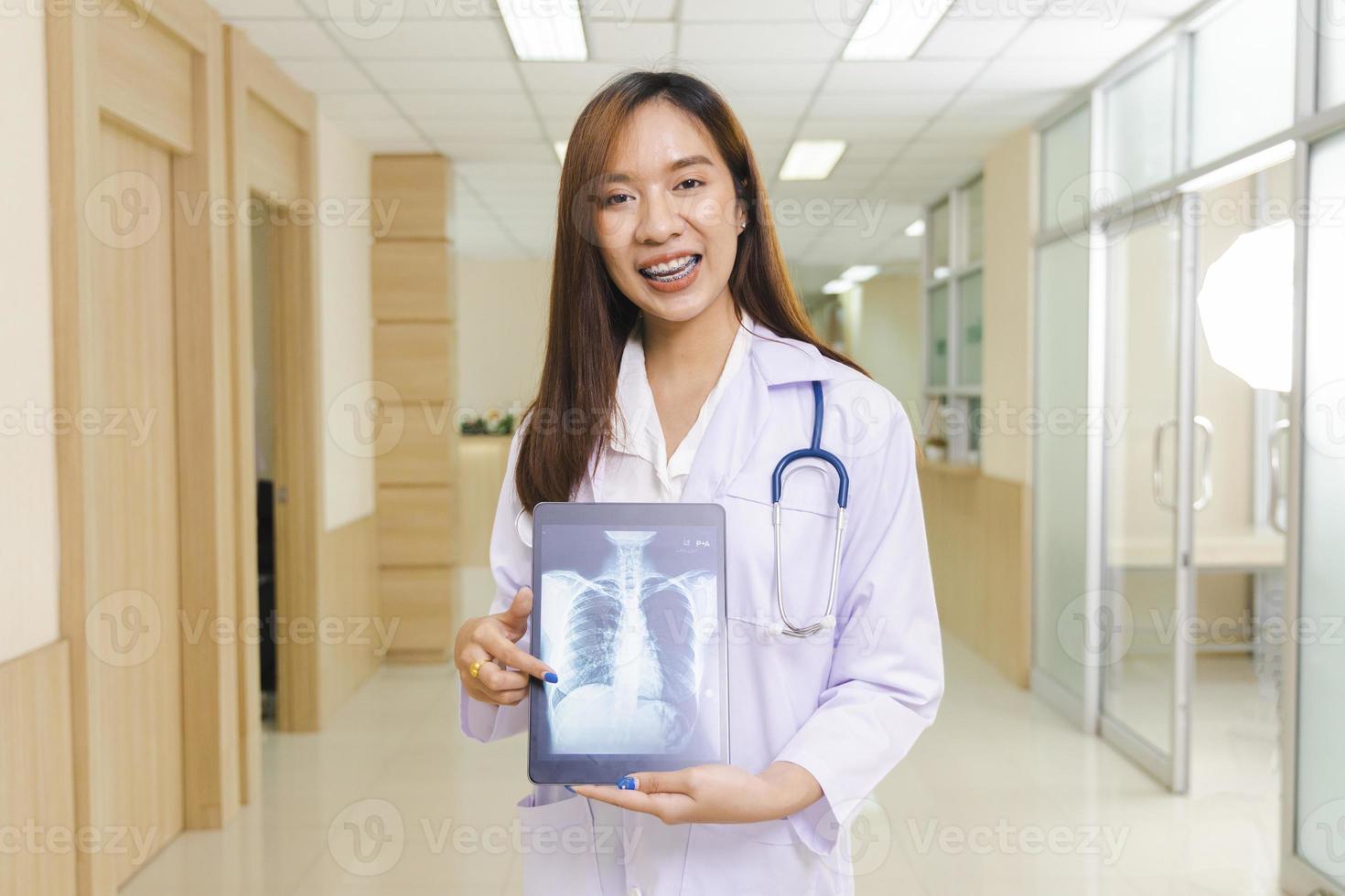 portrait of smart female doctor holding tablet to show X-Ray picture and standing at reception of the hospital. photo