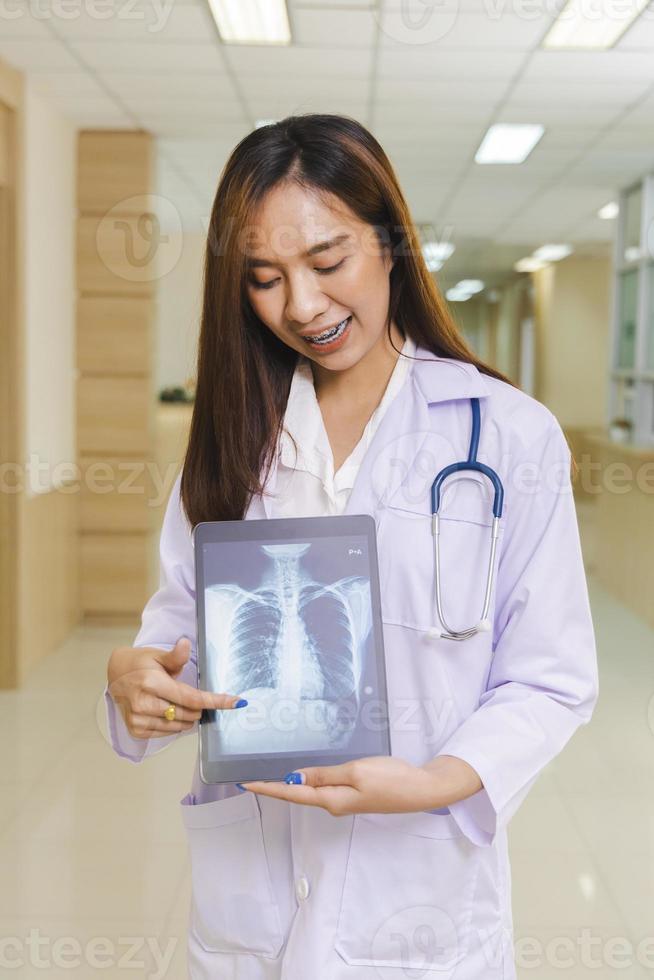 portrait of smart female doctor holding tablet to show X-Ray picture and standing at reception of the hospital. photo