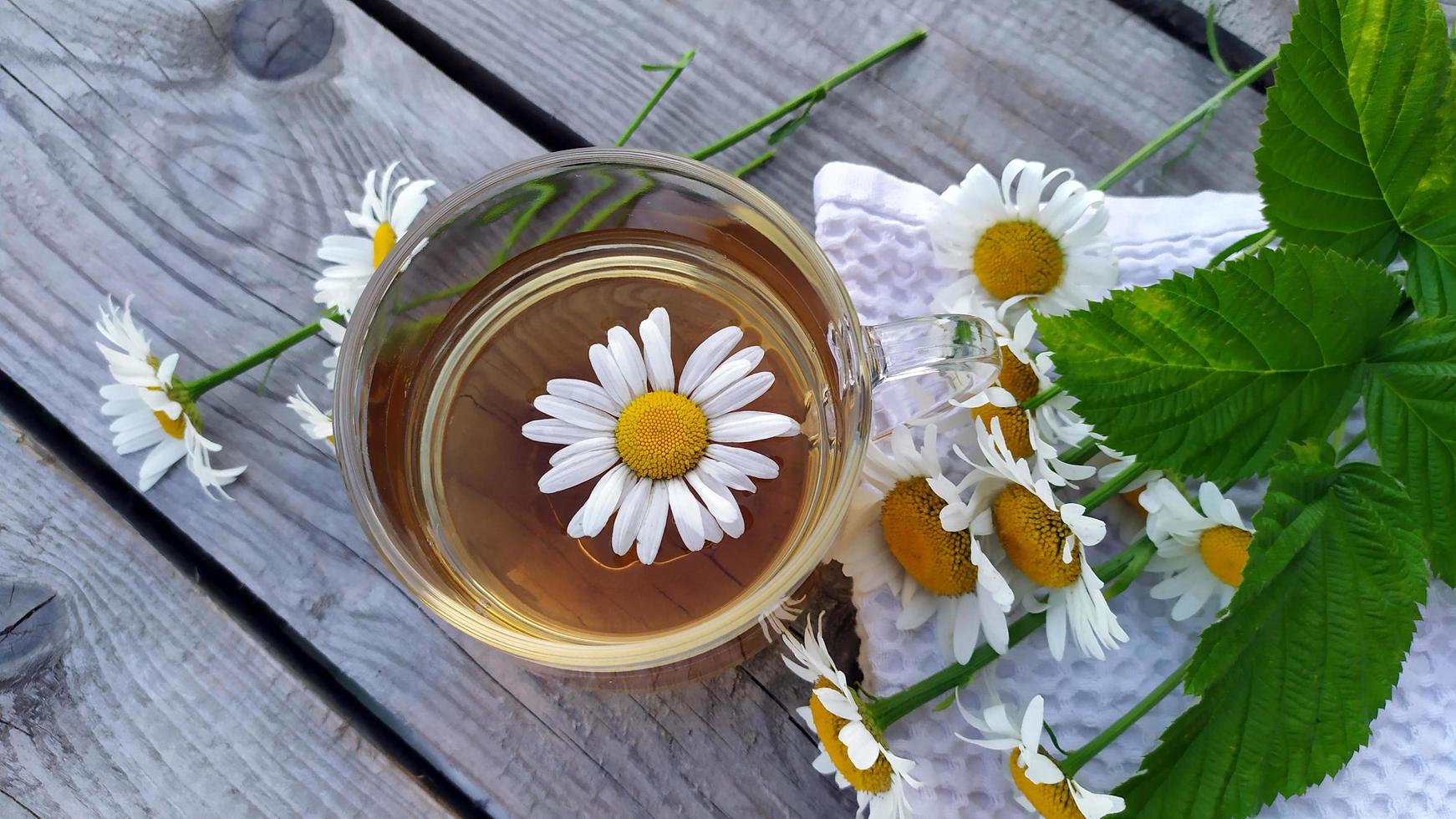 Chamomile tea close-up on a wooden background. Summer still life with wildflowers and chamomile drink in a glass cup. Floral background. View from above. photo