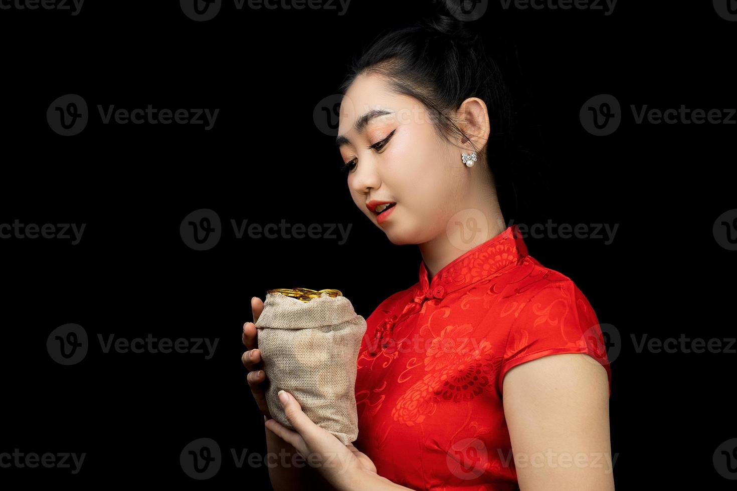 Portrait Asian young, woman red dress traditional cheongsam holding a gold coin in a sack at the black background photo