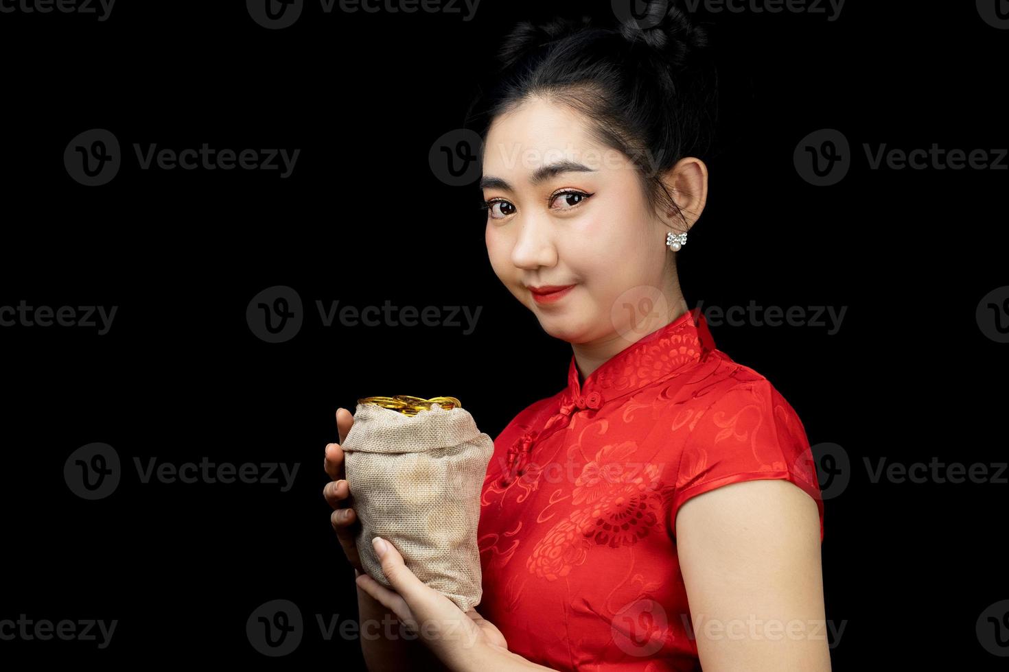 Portrait Asian young, woman red dress traditional cheongsam holding a gold coin in a sack at the black background photo