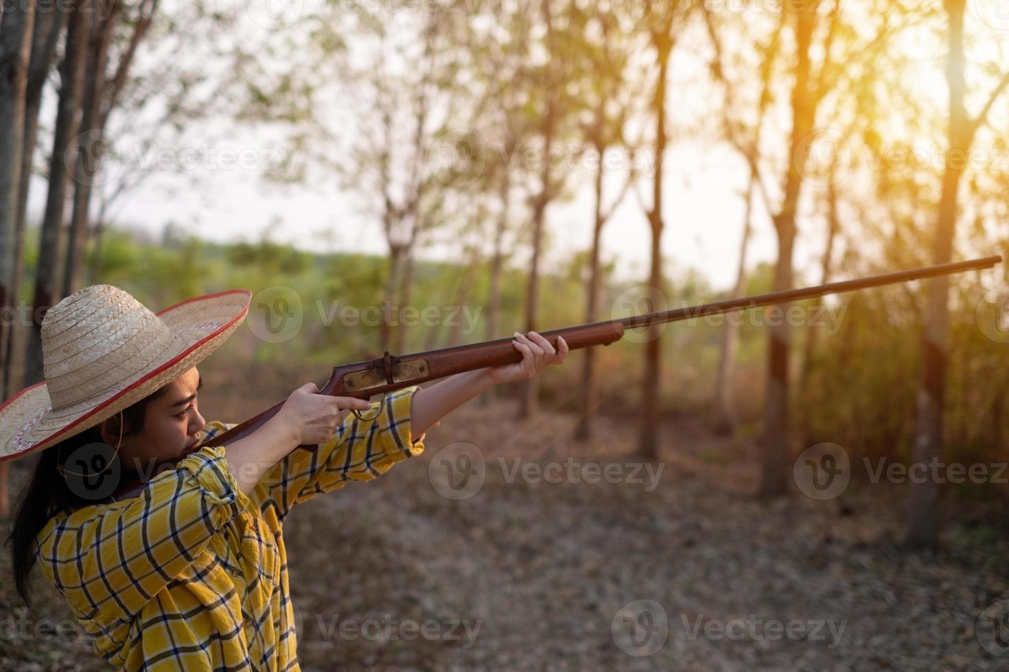 Portrait the farmer asea woman wearing a hat at the shooting range shot from a muzzle-loading vintage gun in the farm, Young girl standing in the attitude of aiming and looking through the sight rifle photo