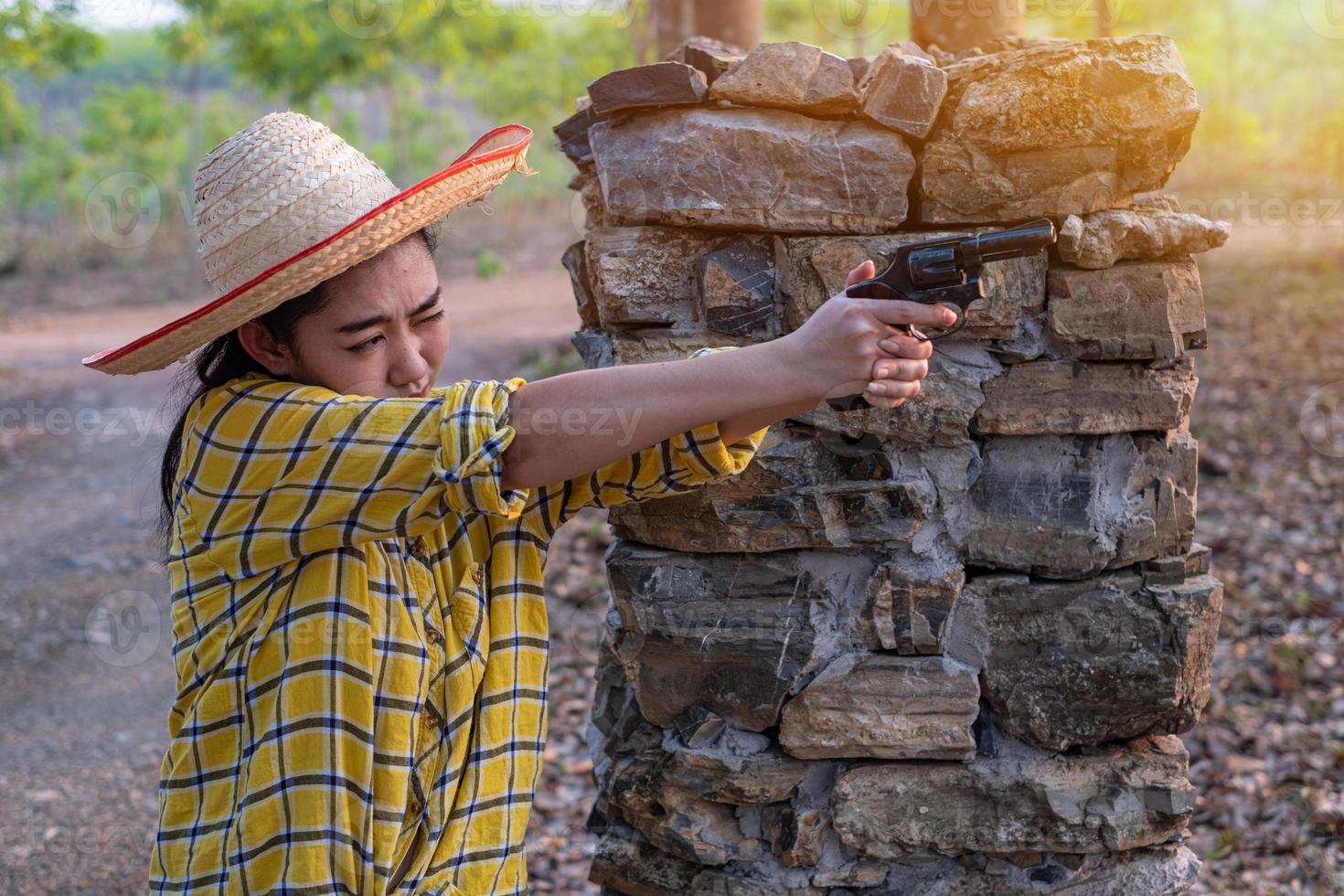 retrato, el, granjero, asea, mujer, con, sombrero, en, el, tiro, tiro, de, viejo, revólver, arma de fuego, en la granja, niña joven, sentado, en, actitud, de, apuntar, y, mirar, por, el, vista, pistola foto