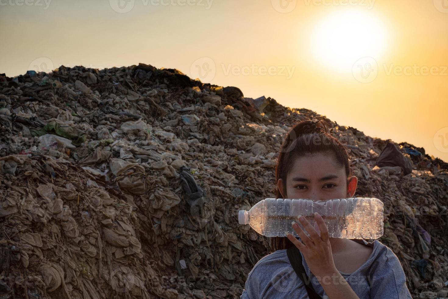 Woman Hand holding use a clear plastic bottle to cover the face at mountain large garbage background photo