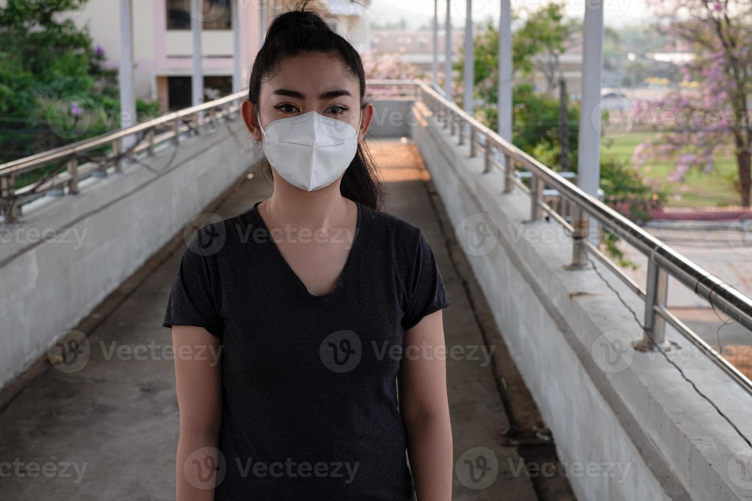 Cerca de una mujer de pie colocándose un respirador n95 máscara para protegerse de enfermedades respiratorias transmitidas por el aire como la gripe covid-19 coronavirus ébola pm2.5 polvo y smog en la carretera fondo con rebabas foto