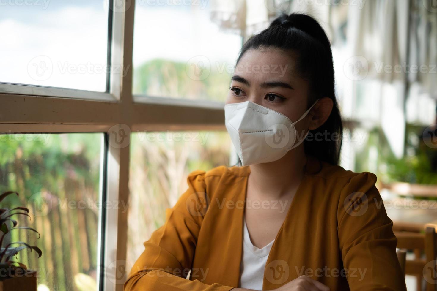 Asia joven mujer sentada y poniéndose una máscara médica para protegerse de la infección por virus, enfermedades respiratorias transmitidas por el aire en el café foto