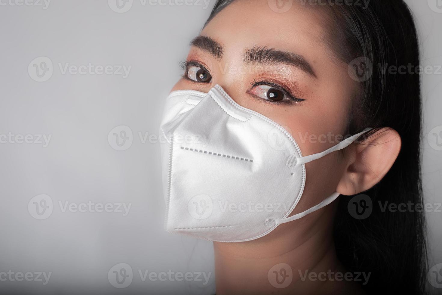 Cerca de una joven mujer asiática poniéndose una mascarilla médica para protegerse de enfermedades respiratorias transmitidas por el aire como la gripe covid-19 pm2.5 polvo y smog en fondo gris, concepto de infección por virus de seguridad foto