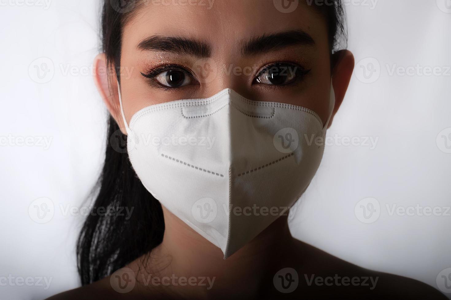 Close up of young Asia woman putting on a medical mask n95 to protect from airborne respiratory diseases as the flu covid-19 PM2.5 dust and smog at gray background, Safety virus infection concept photo