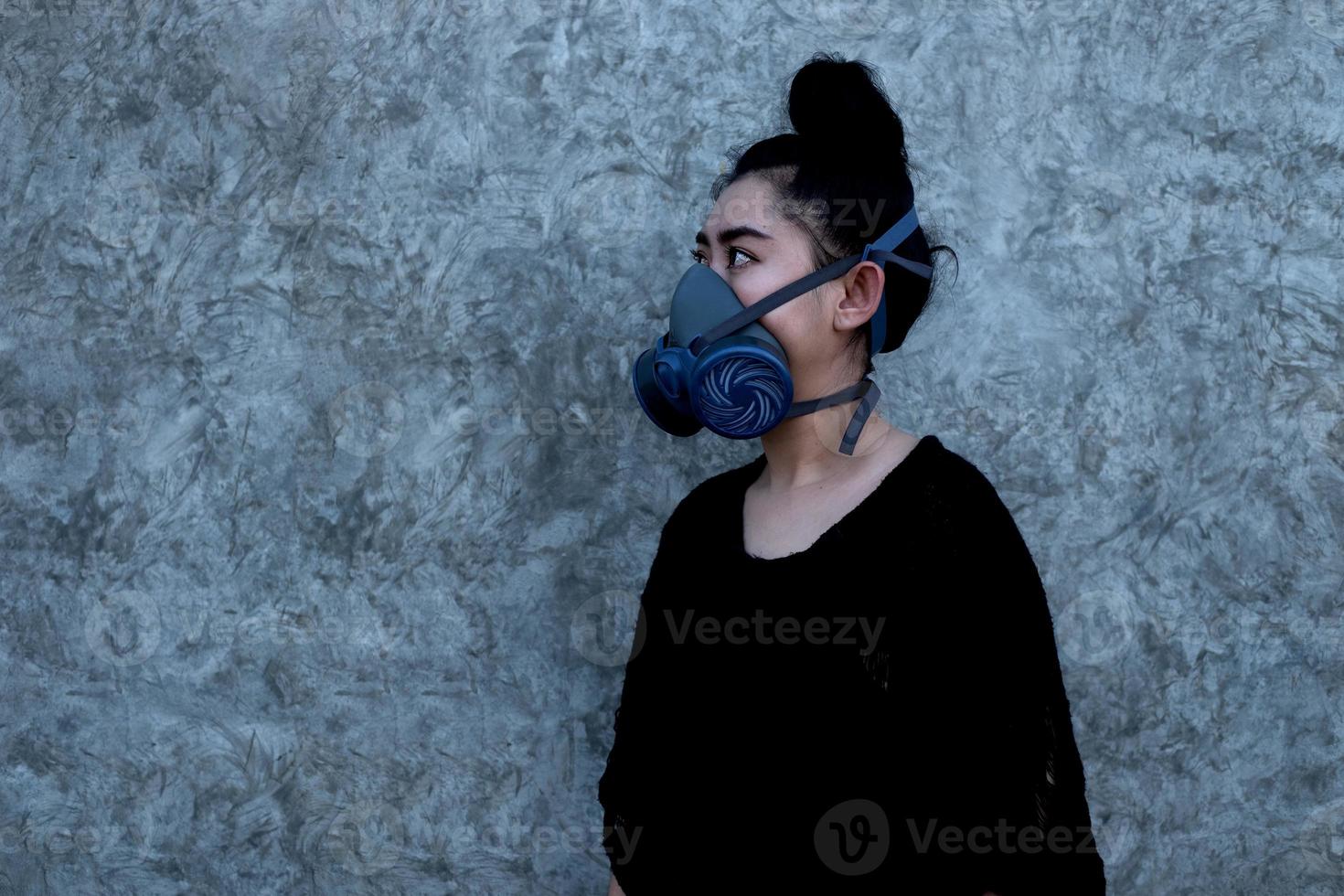 Retrato joven mujer de Asia poniéndose una media máscara respirador con filtro de partículas reemplazables en el fondo de la pared de hormigón con espacio de copia foto