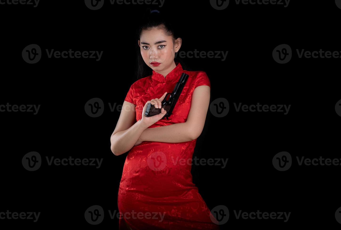 Portrait of a beautiful young Asia woman red dress traditional cheongsam holding gun at the black background photo