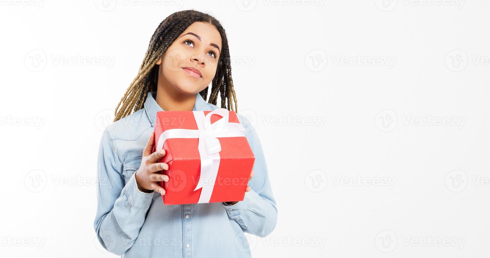 hermosa joven en camisa de mezclilla tiene una caja de regalo grande y mira hacia arriba sobre un fondo blanco. foto