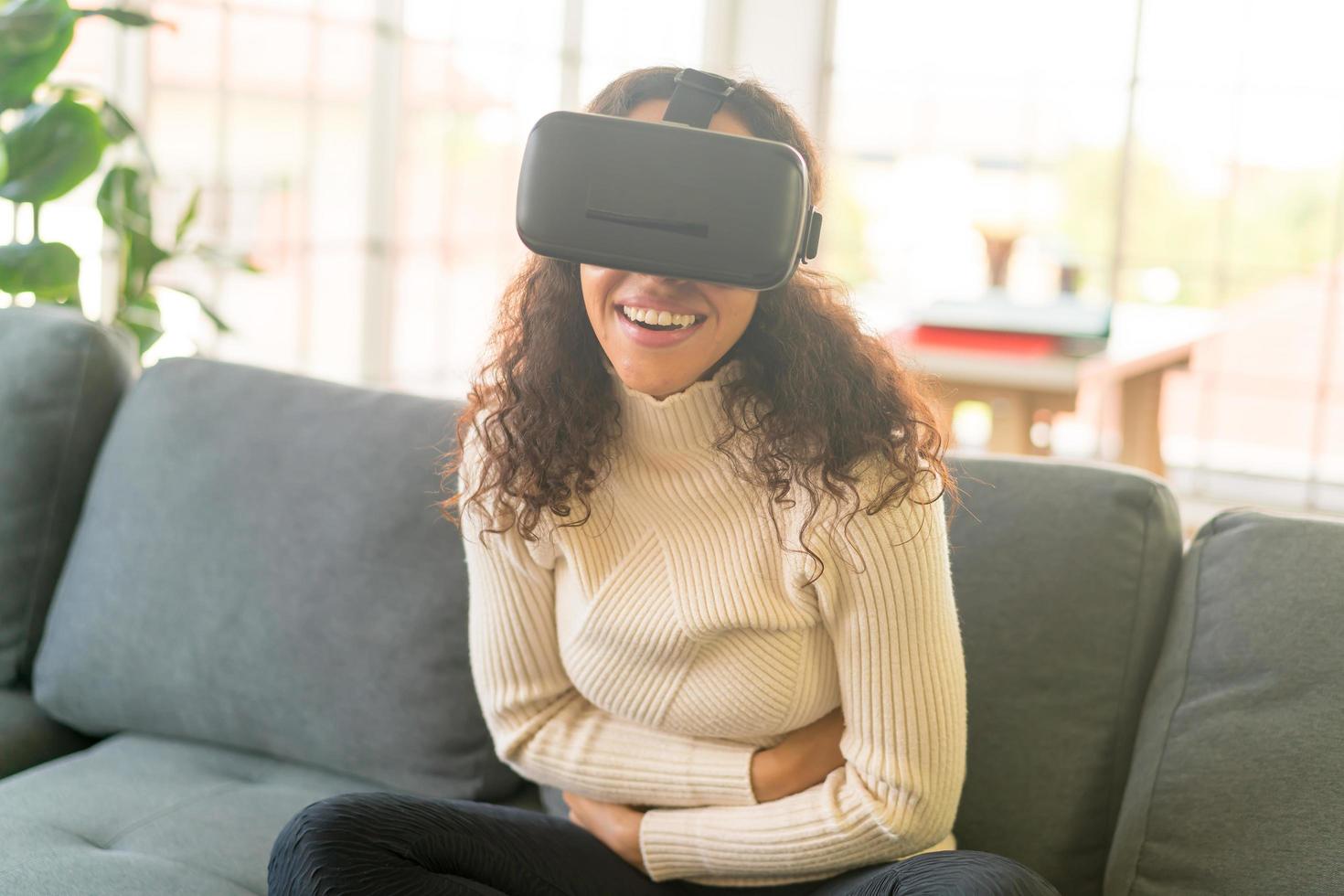 Mujer latina con un casco de realidad virtual en el sofá foto