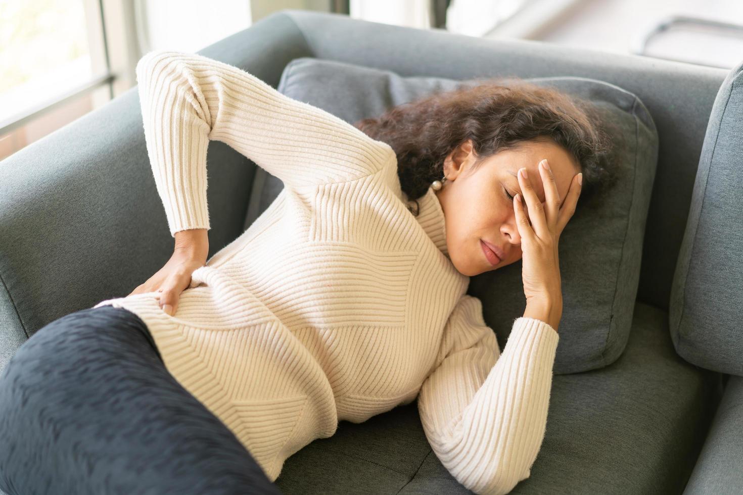 Latin woman lying down on sofa with backache feeling photo