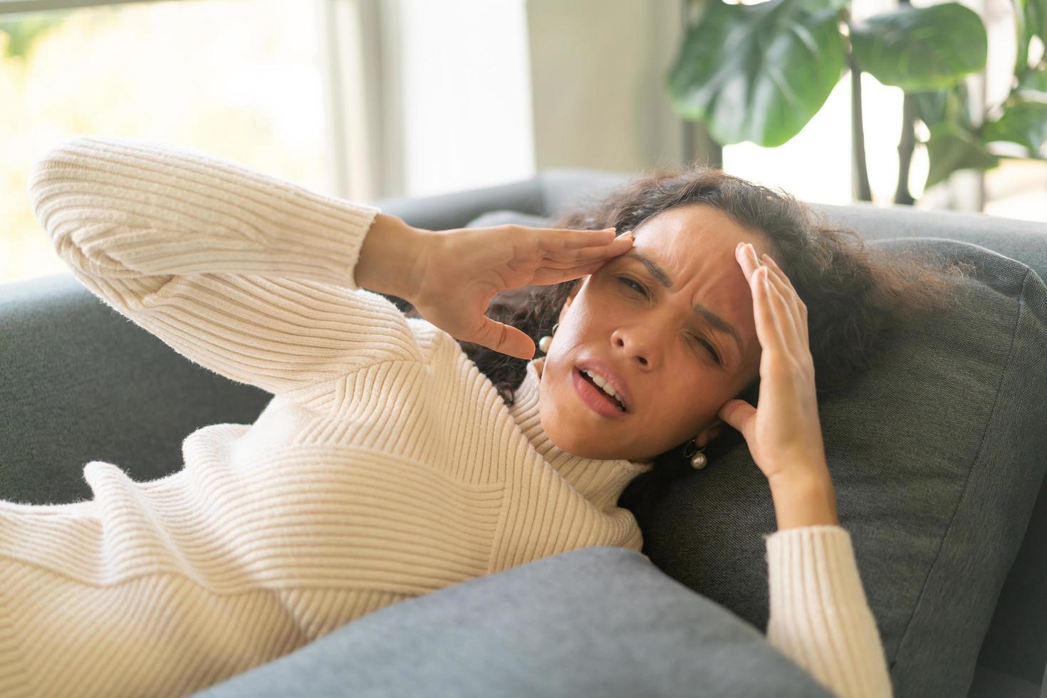 Latin woman lying down on sofa with headache feeling photo