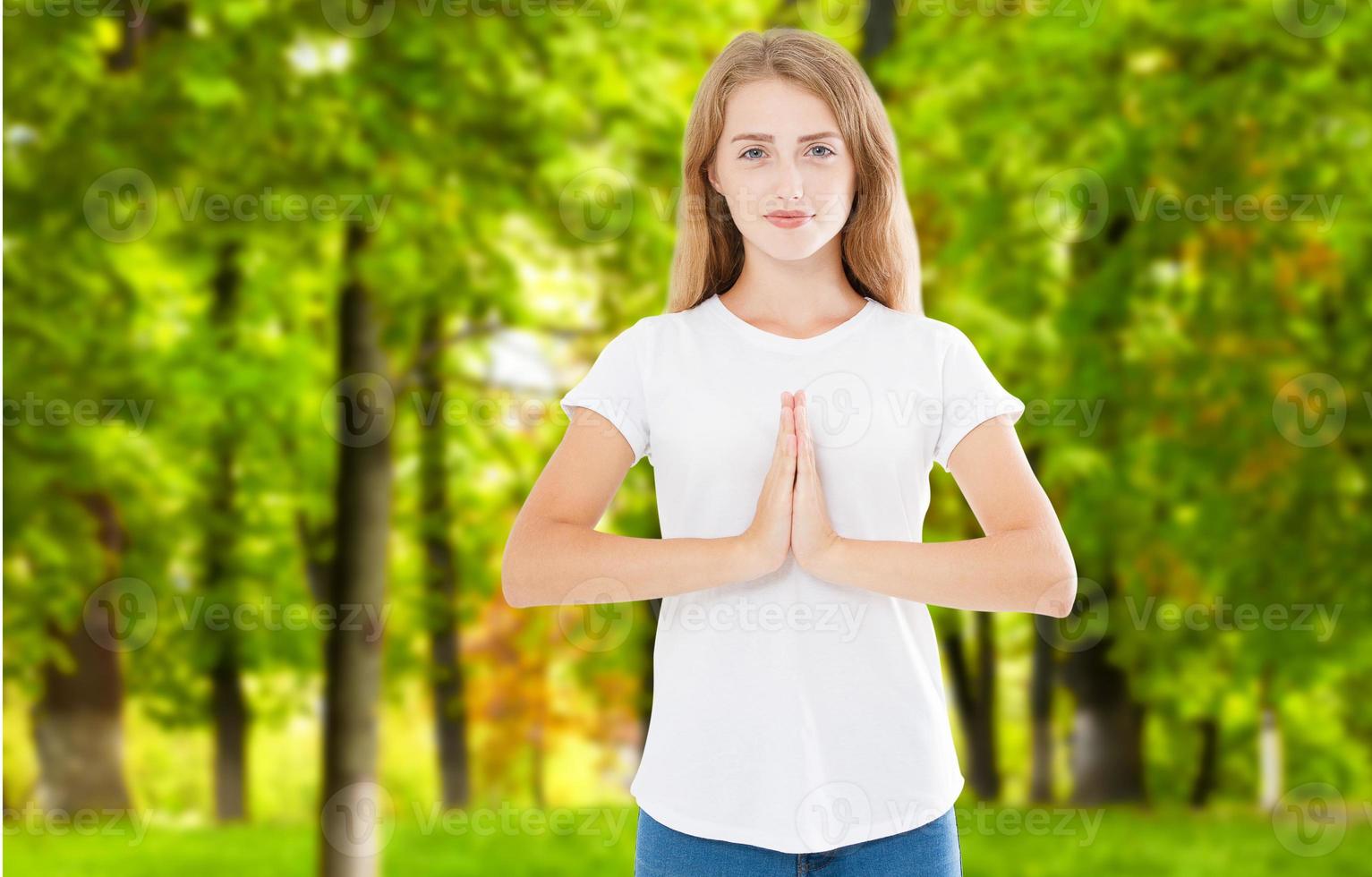 Gorgeous young Caucasian female wearing her ginger, holding hands in namaste or prayer, keeping eyes opened while practising yoga and meditating at park alone, having calm look on her face photo