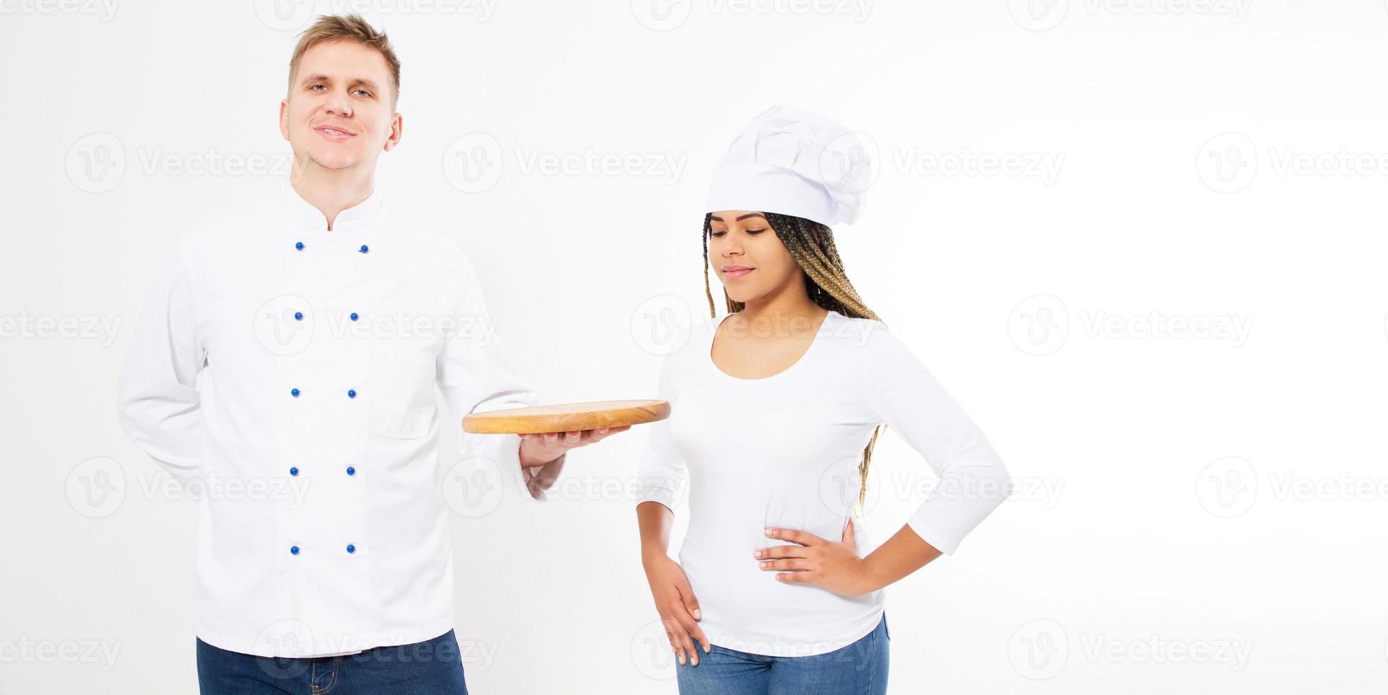 Two teen chefs holding an empty pizza board isolated on white. White and afro american cookers in uniform. photo