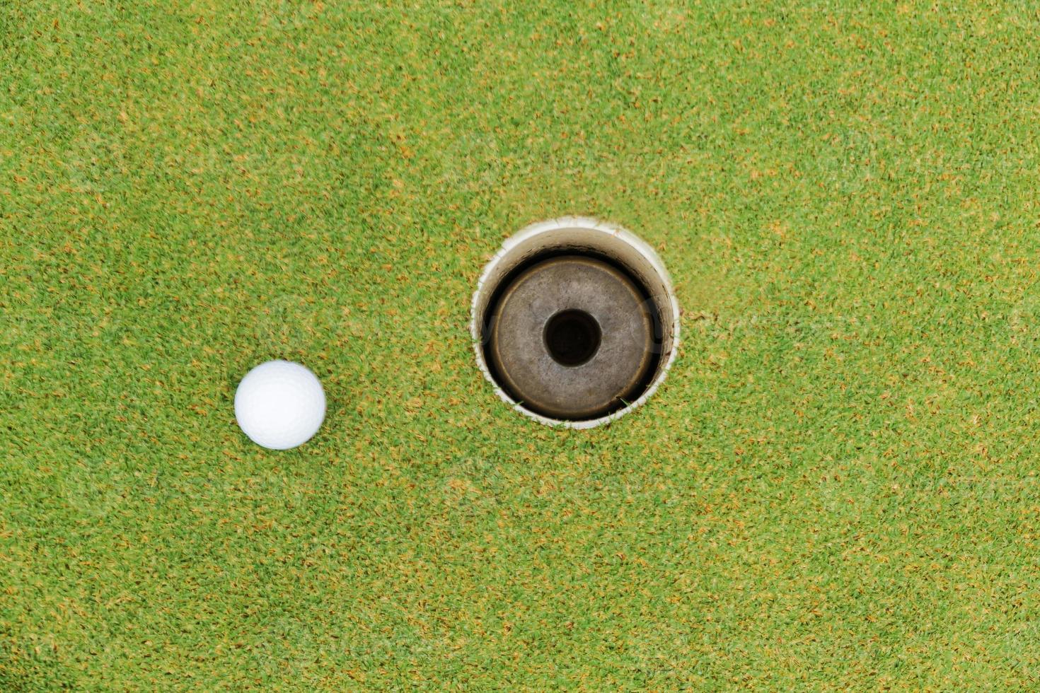 Golf hole and golf ball on green grass on golf course photo