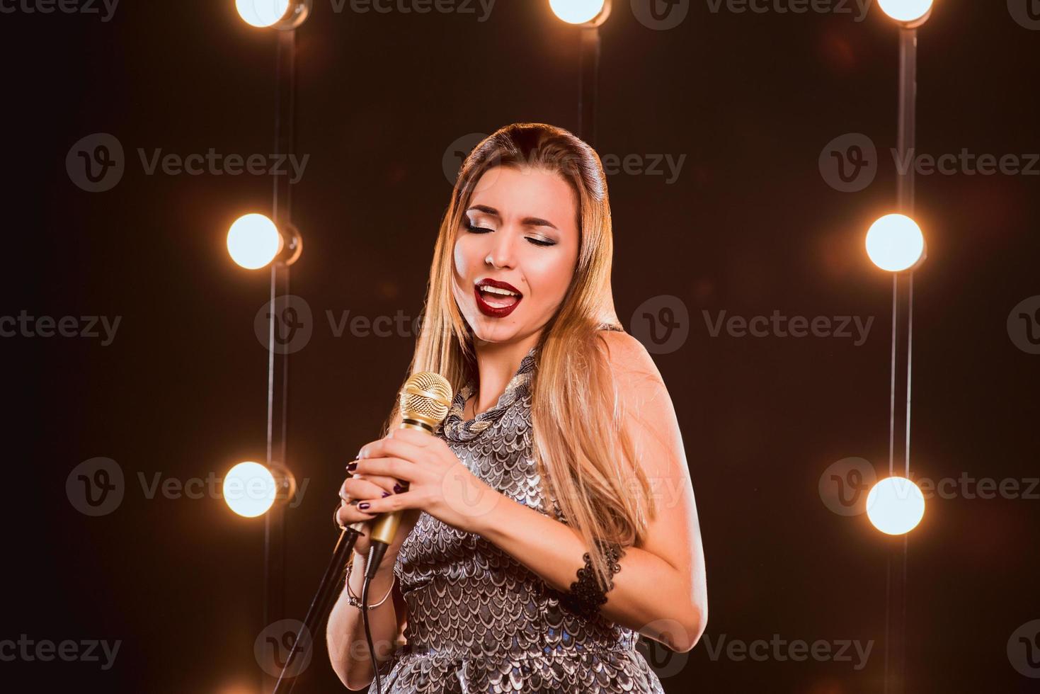 Sonriente joven hermosa chica de pelo largo con micrófono cantando una canción en el escenario de karaoke foto