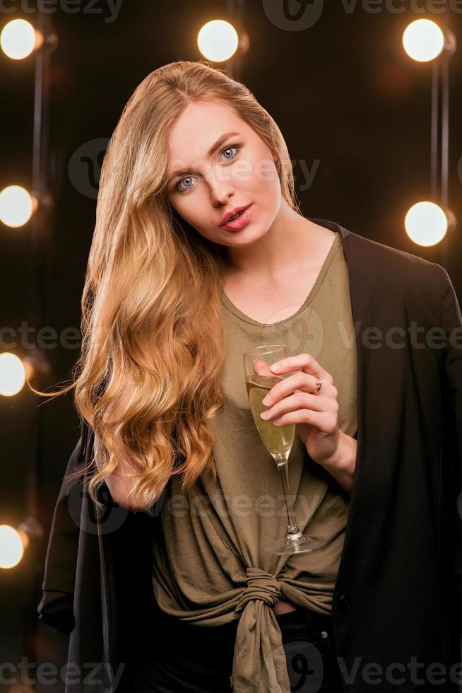 young blonde attractive woman in t-shirt and suit with glass of white sparkling wine on the stage photo