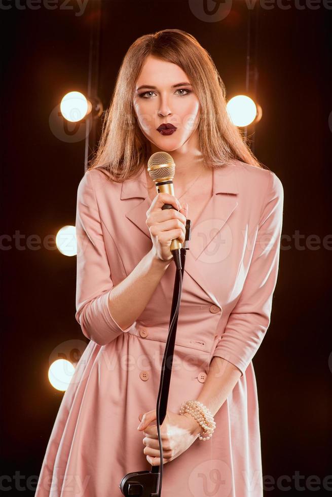 young smiley beautiful long hair girl with microphone singing song on the stage in karaoke photo