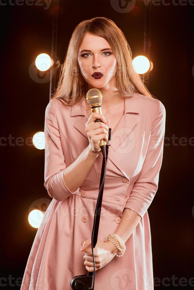 Sonriente joven hermosa chica de pelo largo con micrófono cantando una canción en el escenario de karaoke foto