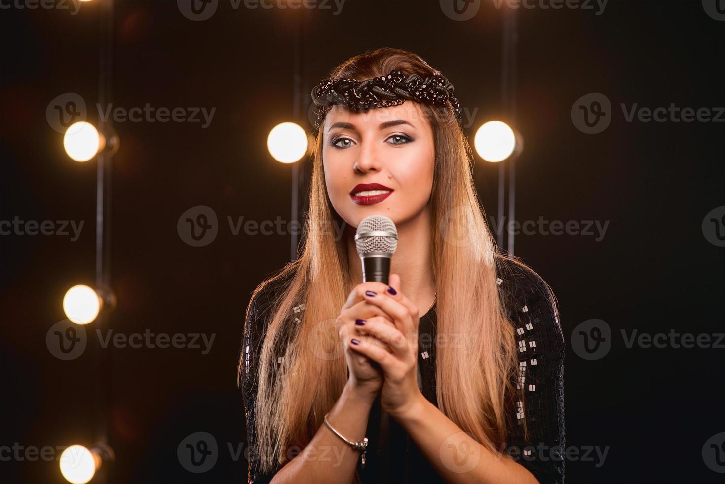 young smiley beautiful long hair girl with microphone singing song on the stage in karaoke photo