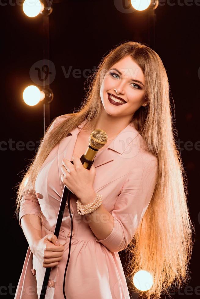 Sonriente joven hermosa chica de pelo largo con micrófono cantando una canción en el escenario de karaoke foto