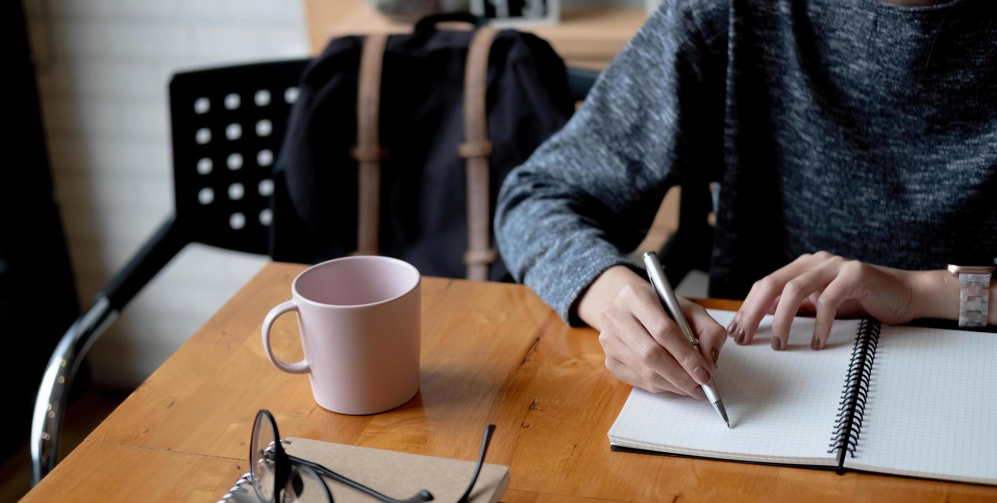 Cropped photo hand of woman writing making list taking notes in notepad working or learning online with laptop at home