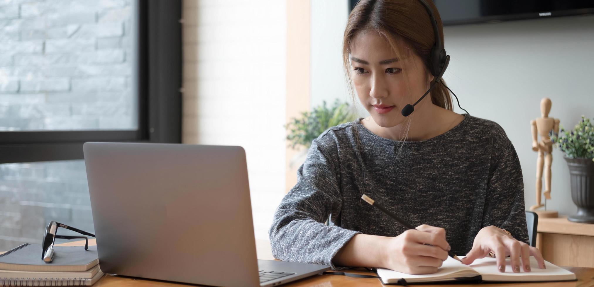 Estudiante asiático tomando notas en el cuaderno y usando una computadora portátil para e-learning, concepto de aprendizaje en línea en el hogar foto