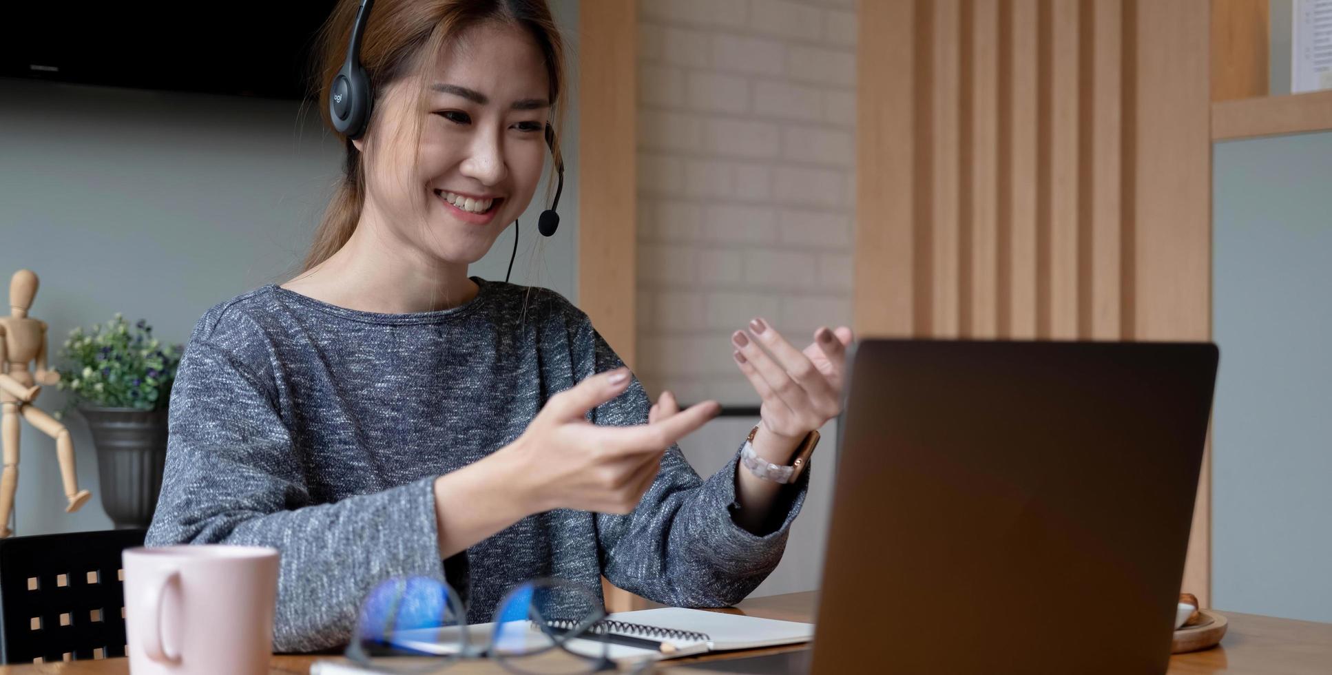 tiro recortado sonriente mujer asiática autónoma con auriculares, comunicándose con el cliente a través de una videollamada por computadora. profesora agradable milenaria dando clases de idiomas en línea foto