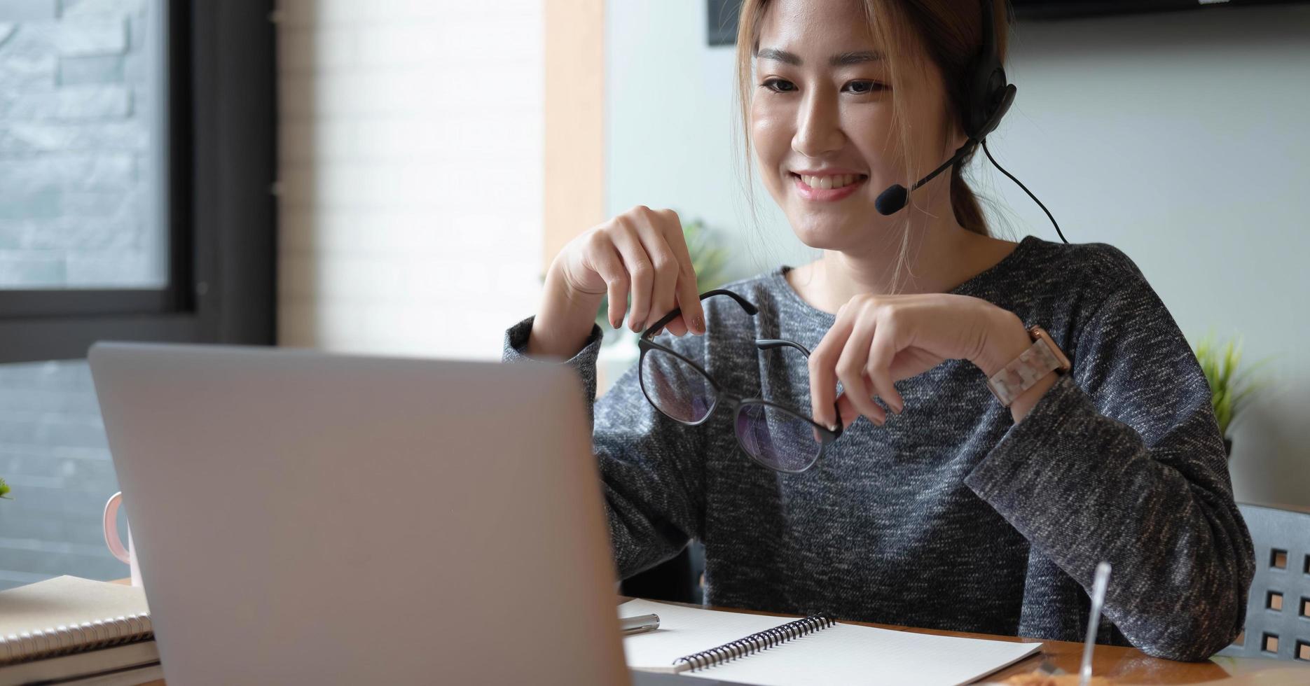 tiro recortado sonriente mujer asiática autónoma con auriculares, comunicándose con el cliente a través de una videollamada por computadora. profesora agradable milenaria dando clases de idiomas en línea foto