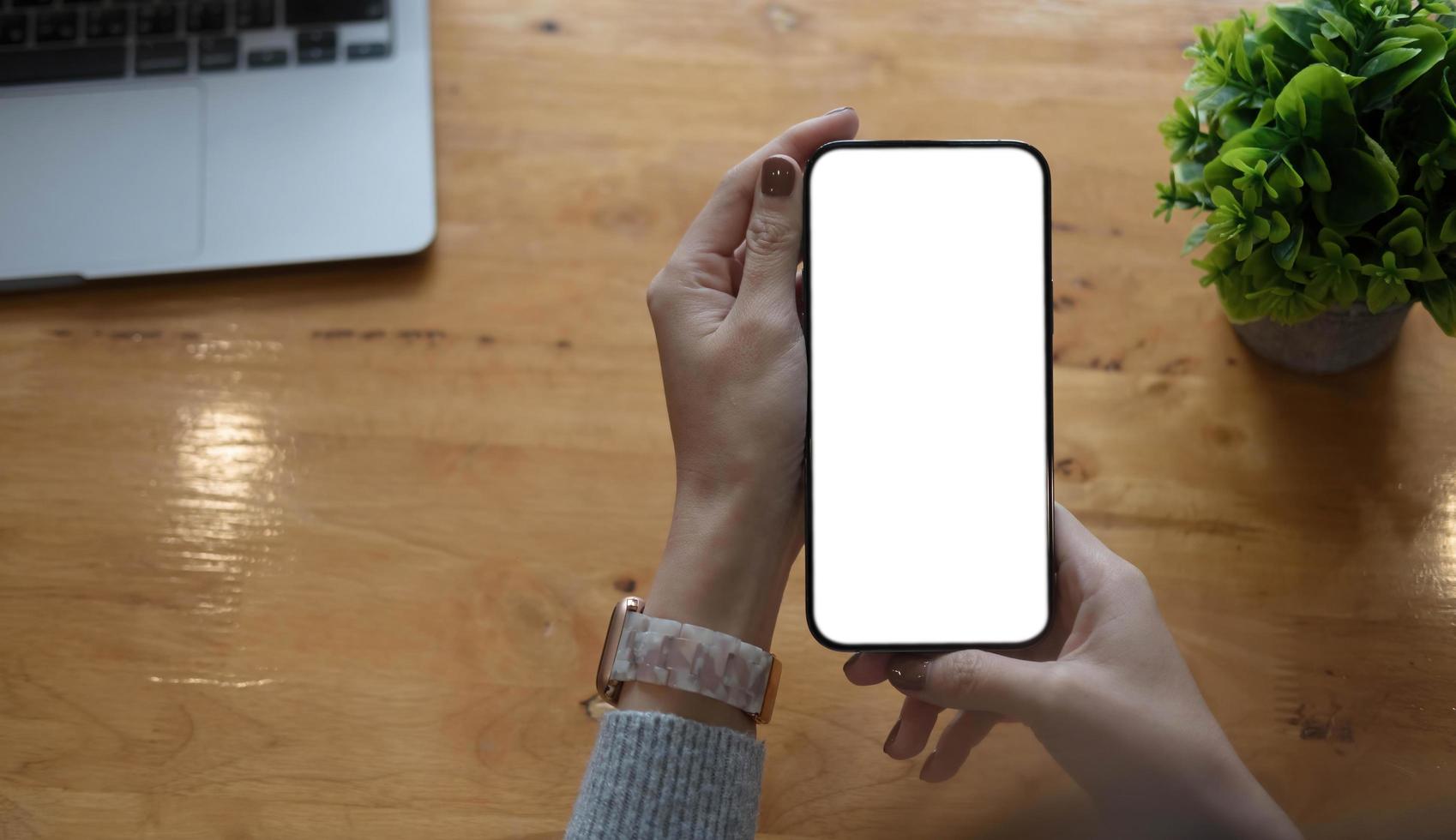 Imagen de maqueta en blanco teléfono celular con pantalla blanca. Mano de mujer sosteniendo mensajes de texto usando el móvil en el escritorio en la oficina en casa. foto