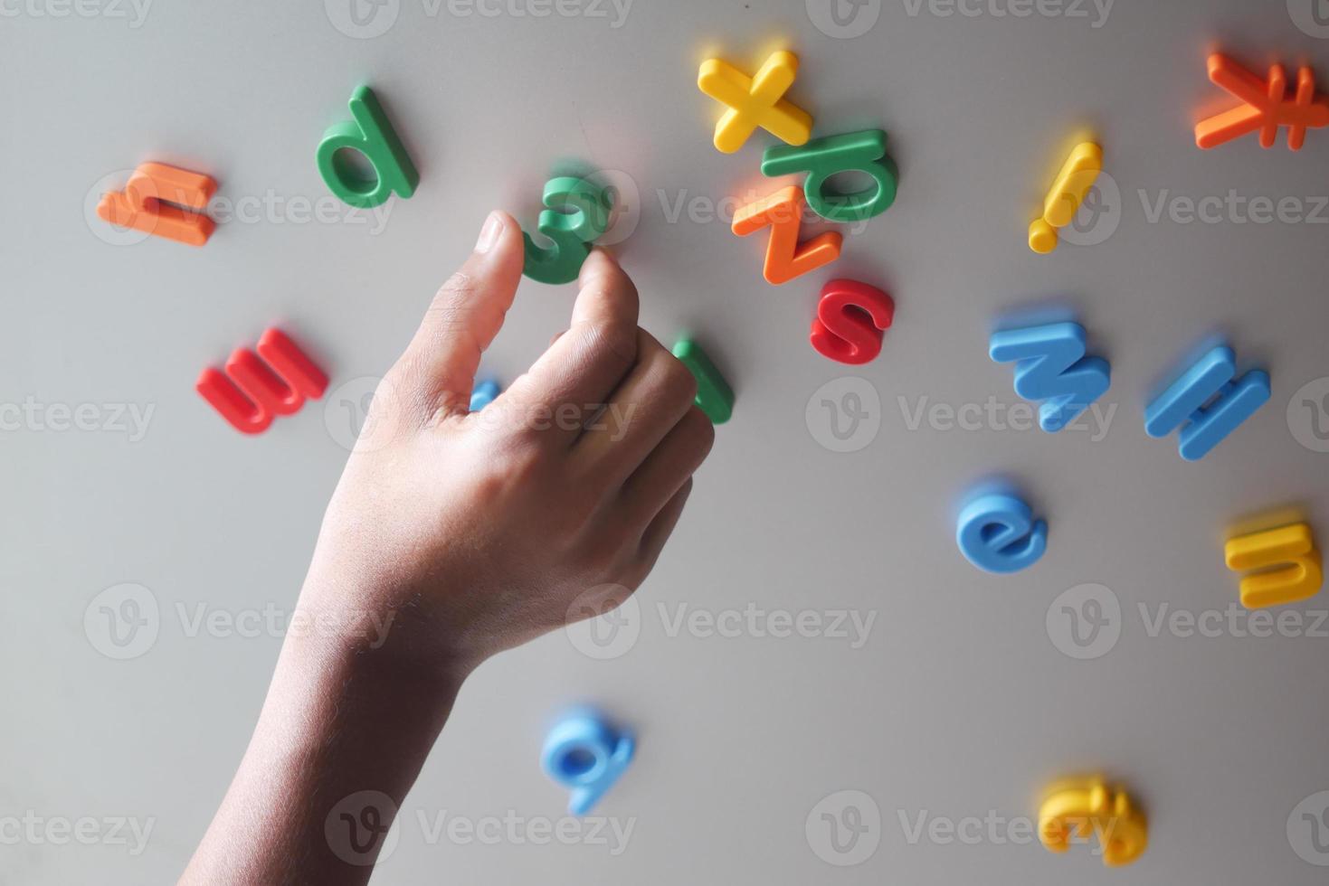 child boy organizing colorful plastic letters on a fridge photo