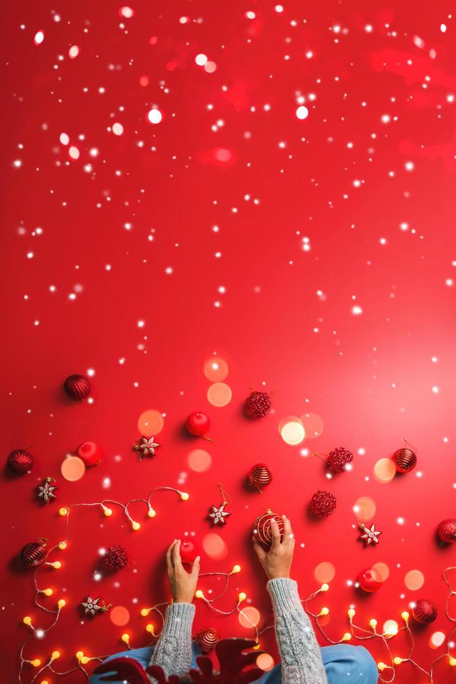 la niña está usando la mano para sostener la bola adornos rojos sobre un fondo rojo con adornos navideños con luz led. vista superior. tradiciones familiares navideñas. concepto de navidad. foto