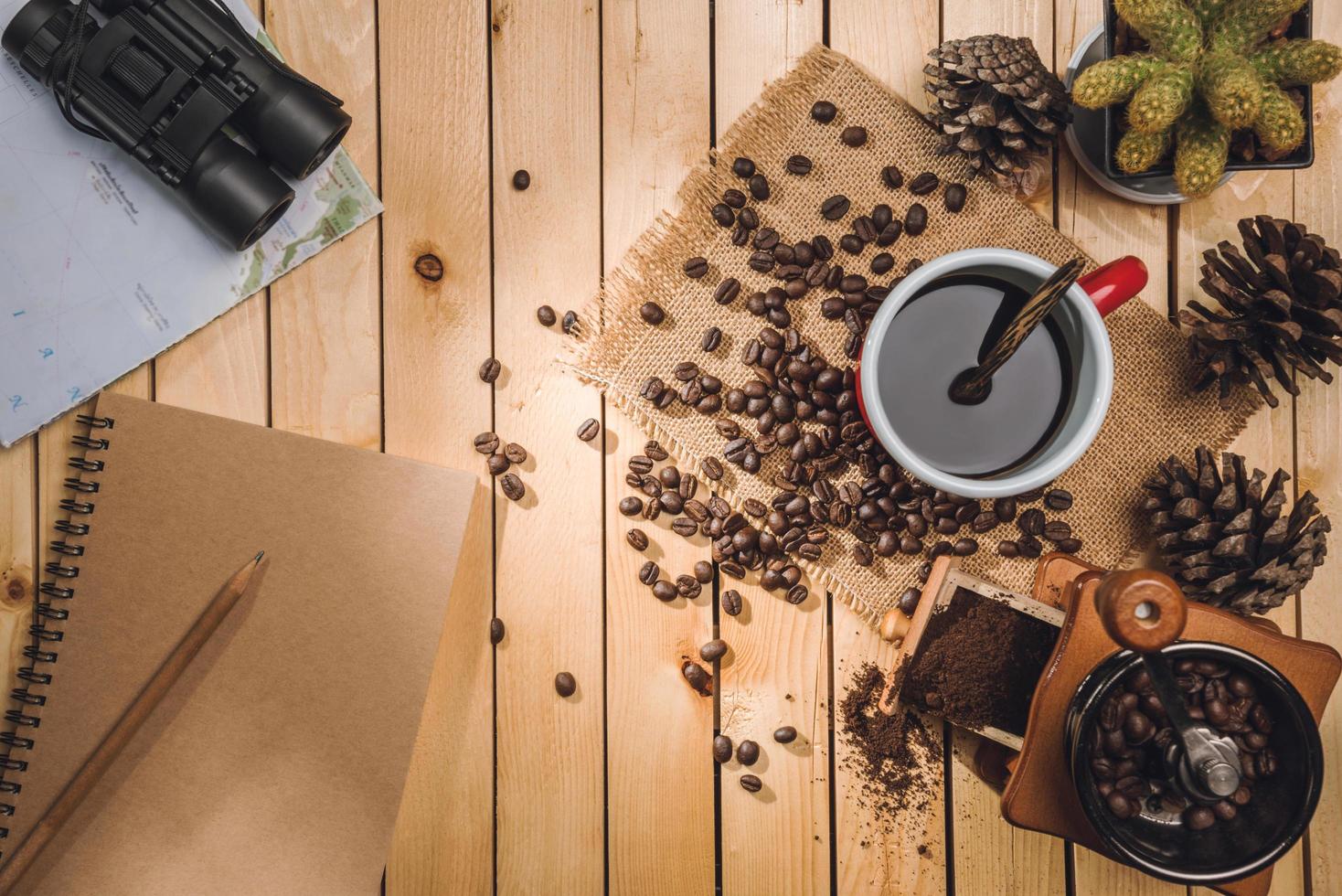 taza de café negro y granos de café, molinillo de café, mapa, binoculares en la mesa de madera foto