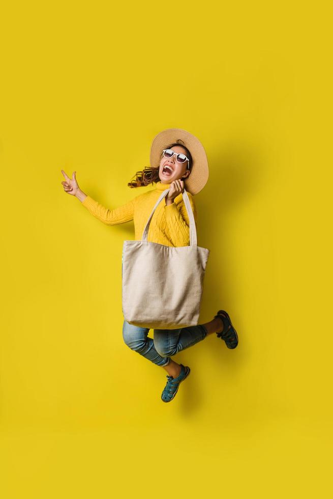 Portrait of an excited beautiful girl wearing dress and sunglasses holding shopping bags. Cheerful young woman with handbag on yellow background. Shopaholic shopping Fashion. photo