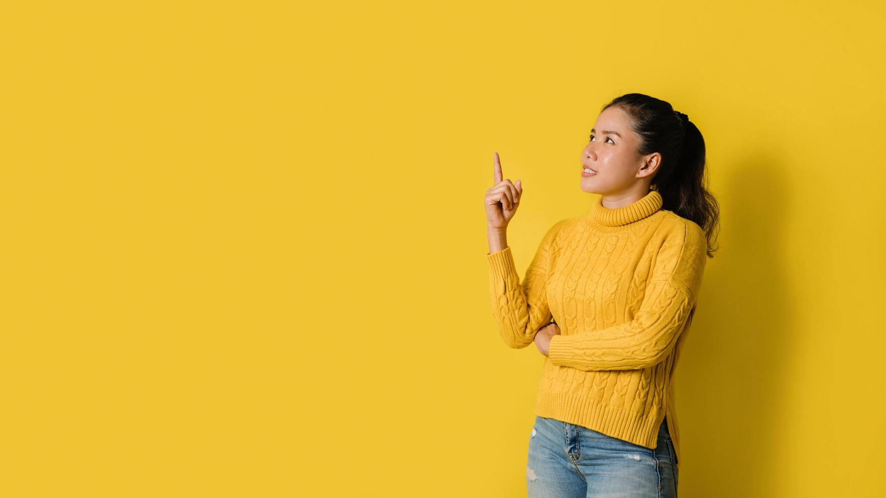 Portrait of an excited young blonde girl pointing with hand and finger to the side looking on yellow background. Pointed to the presentation. Space for text photo