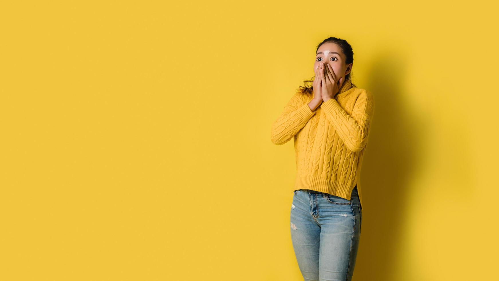 Portrait of a girl shocked raise hands close mouth, with space to copy the text isolated over yellow background. photo