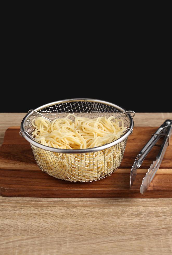 Espaguetis cocidos en recipiente de metal sobre tabla de cortar foto