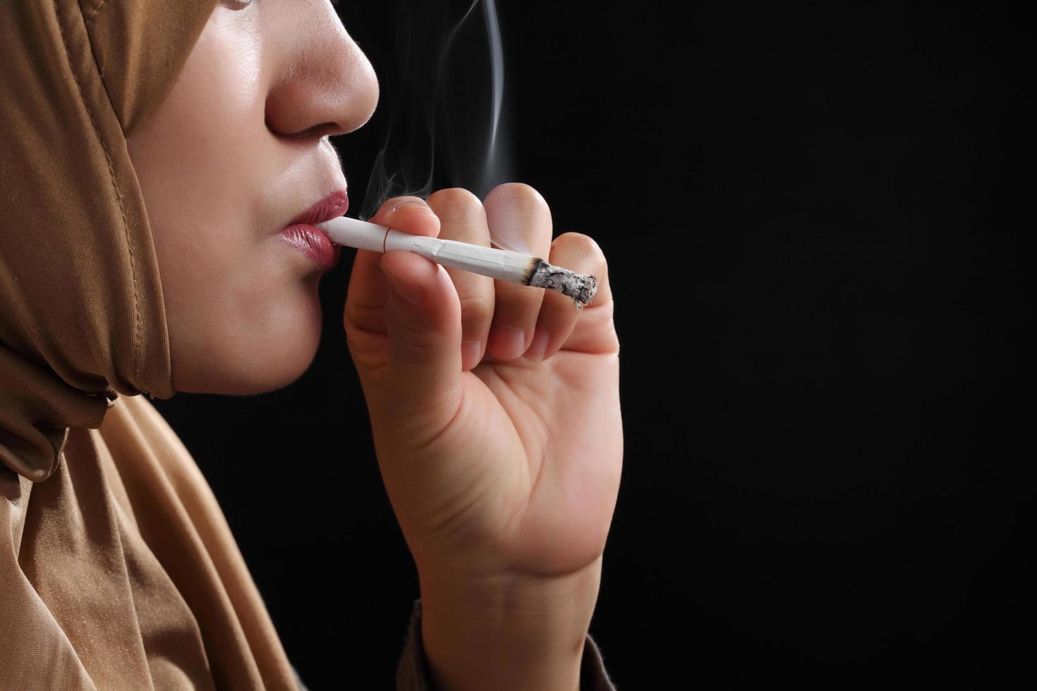 Close up young muslim woman smoking a cigarette on black background photo