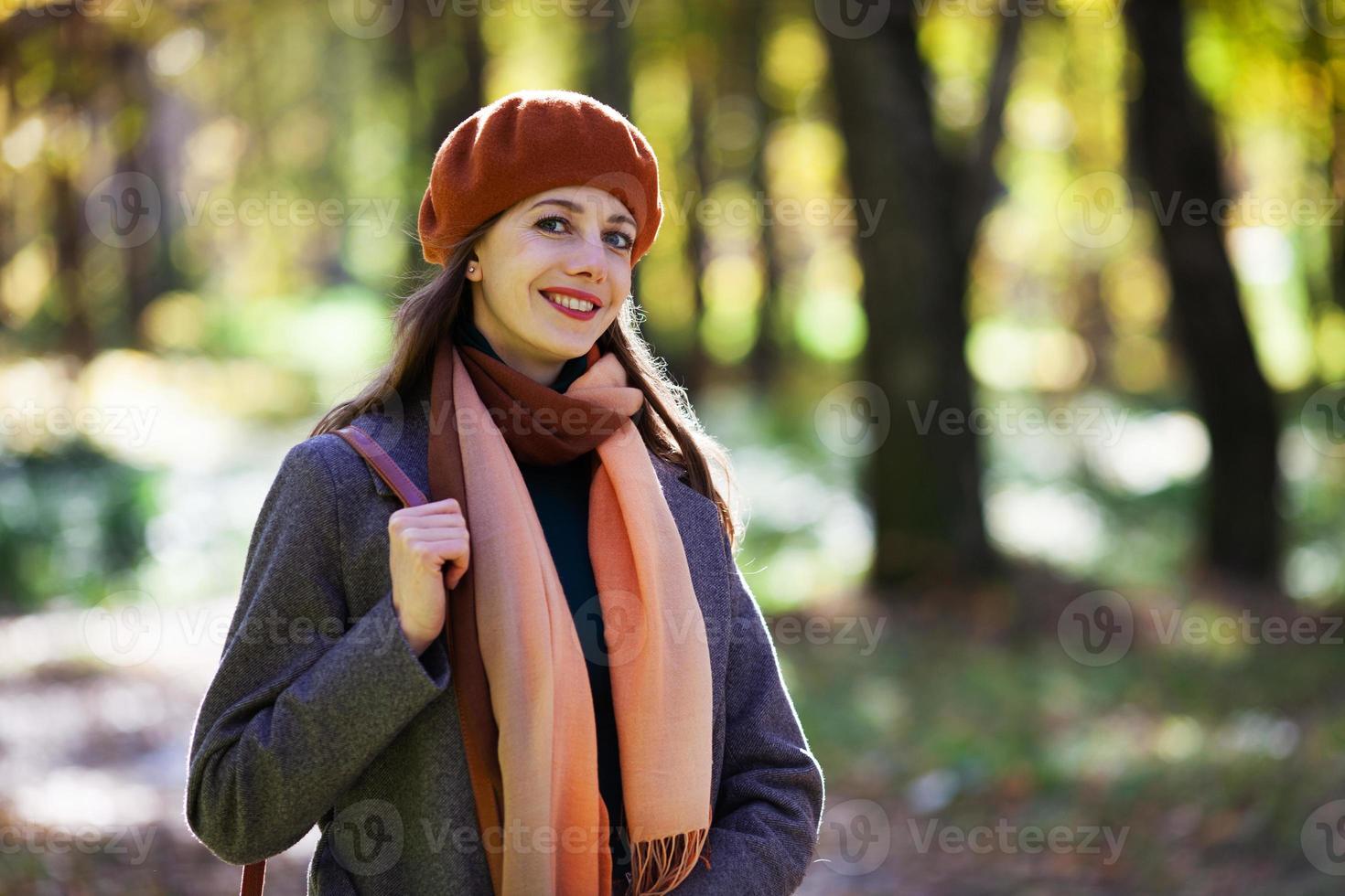 Mujer joven con una boina naranja camina en un parque de otoño foto