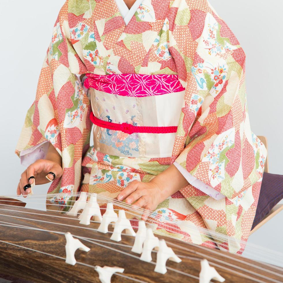 Mujer irreconocible vestida con un kimono tocando un koto, un instrumento de cuerda tradicional japonés. foto