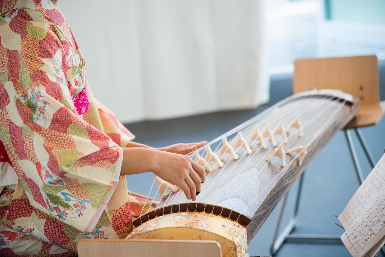 Cerca de un artista japonés con un hermoso kimono y tocando el koto, un instrumento de cuerda tradicional. mujer irreconocible. foto