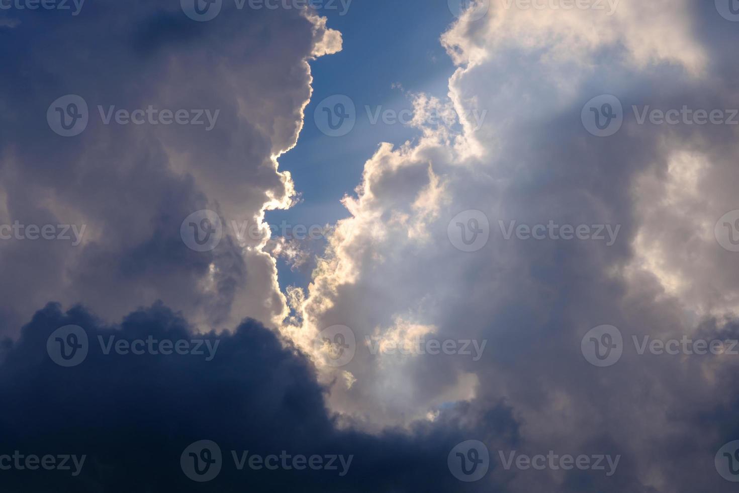 la luz del sol atravesando las nubes blancas y oscuras en el cielo azul foto